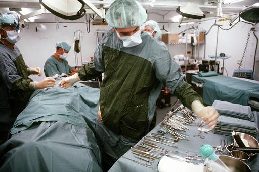 An assistant gets a pair of forceps for the doctor as a surgical team ...